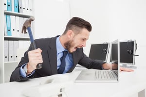 Angry businessman holding hammer over laptop in his office